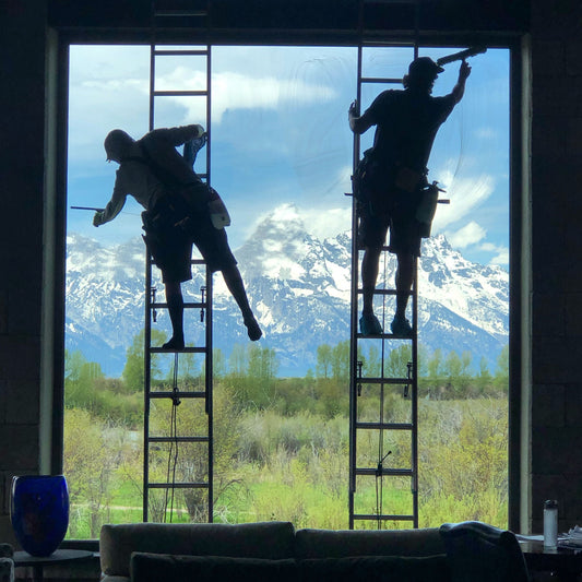 Dual Window Washers Cleaning Large Glass Pain with Mountain Range in Background