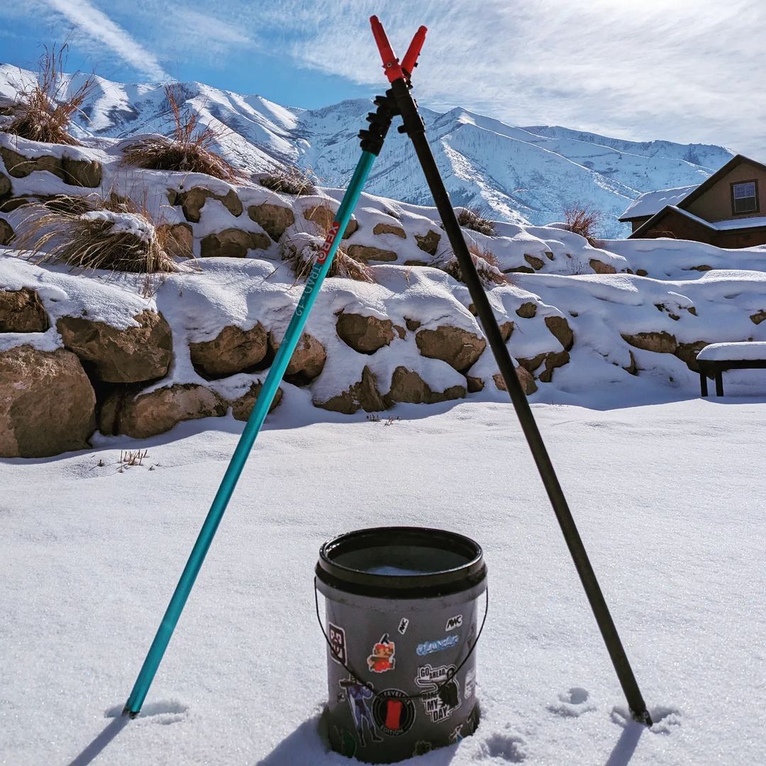 Two Telescopic Trad Poles Standing in Snow with Snows Rocks and Mountains Behind them.