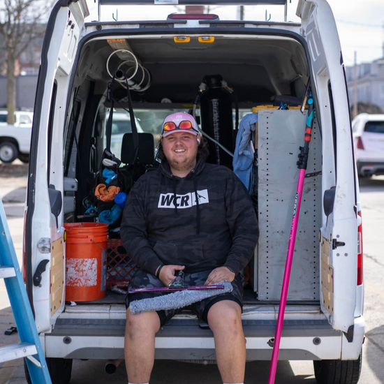 Zayne sitting in the back of a window cleaning van holding window cleaning