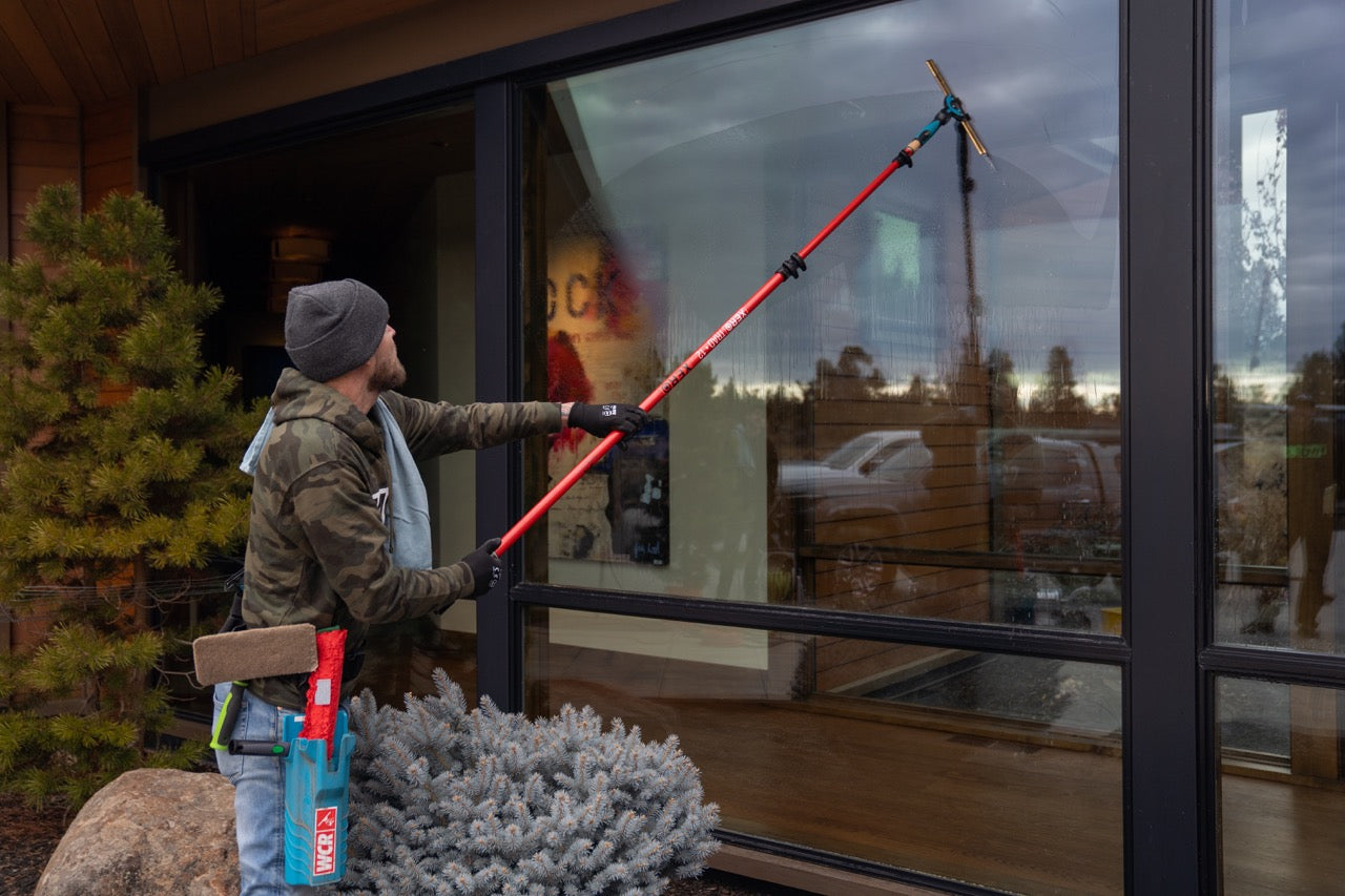 Window Cleaner using a red XERO trad pole with the Ultimate Squeegee Combo on first level commercial building.